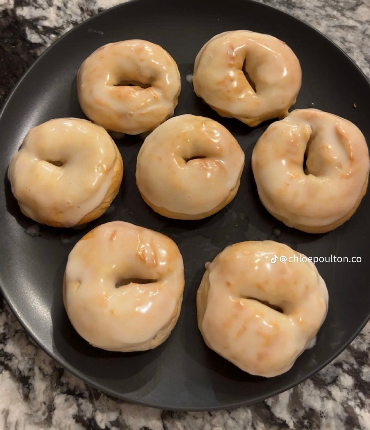 Seven golden doughnuts covered with a glossy glaze on a dark plate